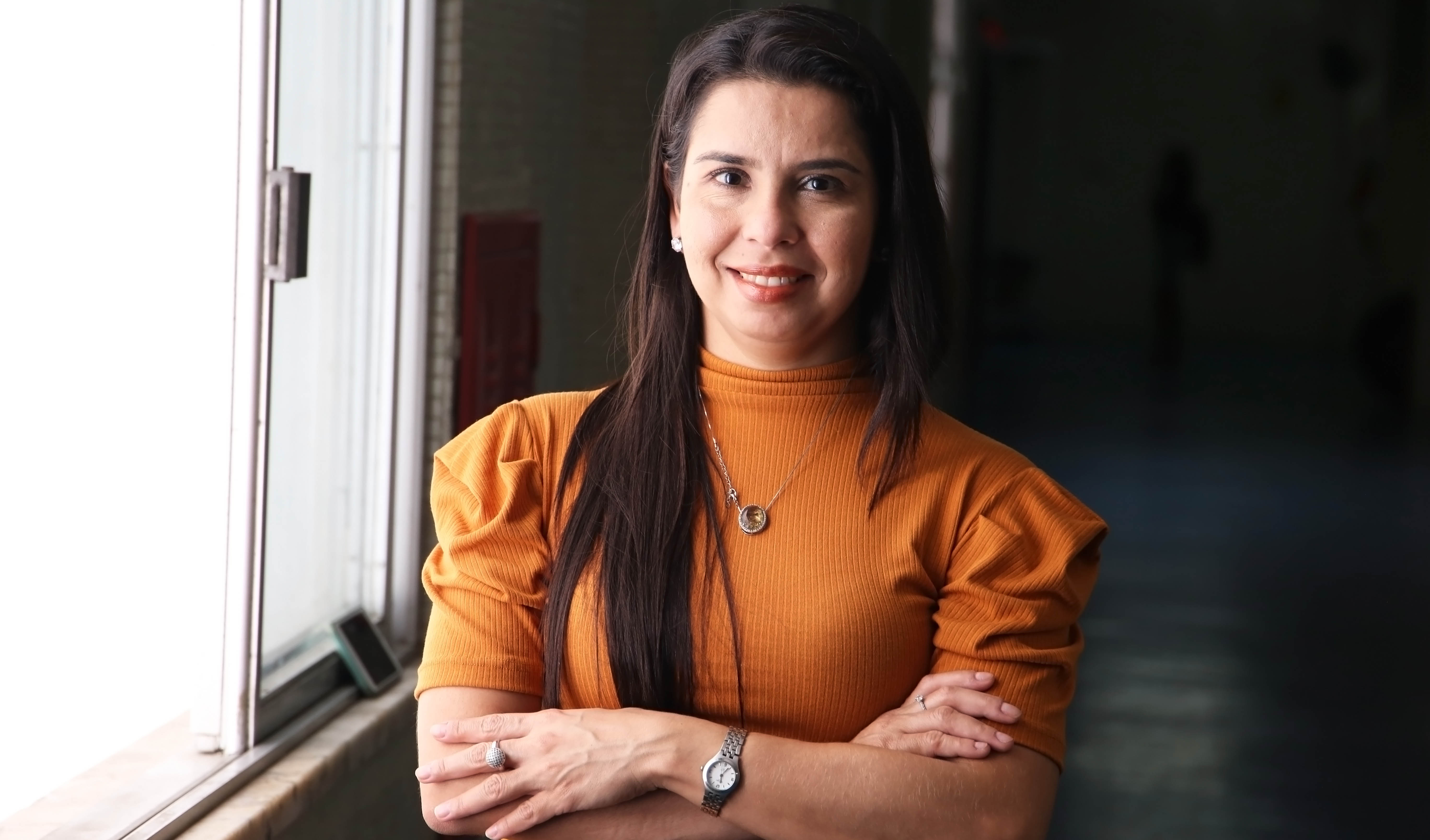 mulher sorrindo para a foto de braços cruzados